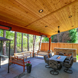 Immagine di un patio o portico american style di medie dimensioni e dietro casa con un caminetto, pavimentazioni in cemento e un tetto a sbalzo