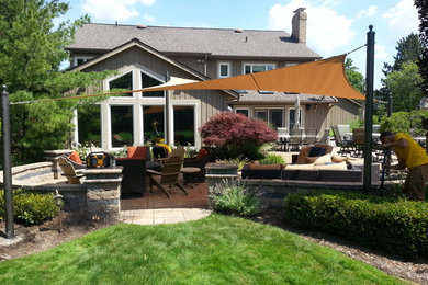 Example of a large trendy backyard stamped concrete patio kitchen design in Cleveland with an awning