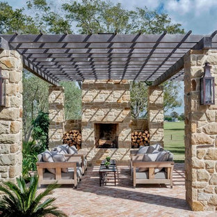 Ispirazione per un grande patio o portico country dietro casa con pavimentazioni in mattoni, una pergola e un caminetto