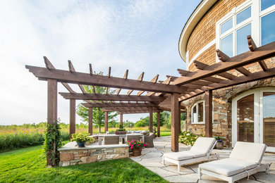 Large mountain style backyard stone patio photo in Minneapolis with a pergola