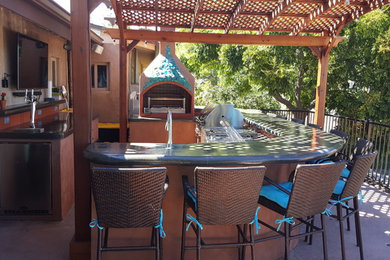 Foto de patio tradicional de tamaño medio en patio trasero con cocina exterior, losas de hormigón y pérgola