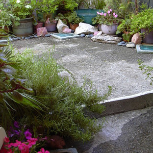 Immagine di un piccolo patio o portico eclettico dietro casa con un giardino in vaso, lastre di cemento e un parasole
