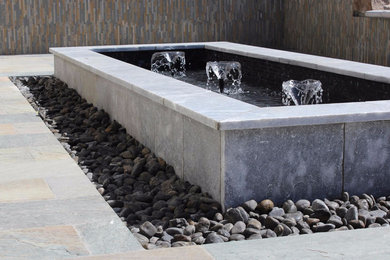 Modelo de patio grande sin cubierta en patio trasero con fuente y adoquines de piedra natural
