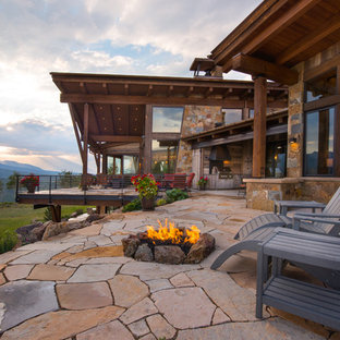 Immagine di un ampio patio o portico stile americano dietro casa con un focolare, pavimentazioni in pietra naturale e un tetto a sbalzo