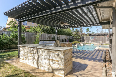 Large transitional backyard stone patio kitchen photo in Houston with a pergola