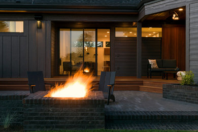 Modern back patio in Portland with a fire feature, brick paving and a roof extension.