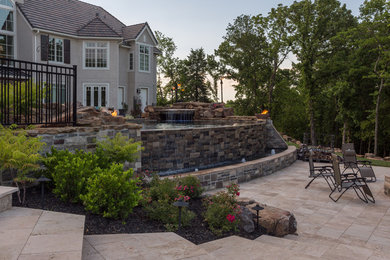 Modelo de patio clásico renovado grande sin cubierta en patio trasero con fuente y adoquines de piedra natural