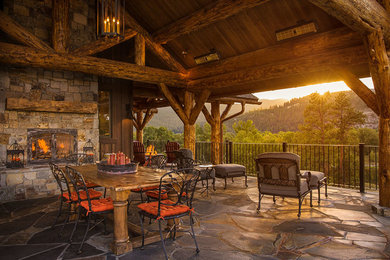Inspiration for a large rustic backyard stone patio remodel in Other with a fire pit and a roof extension