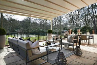 Inspiration for a large modern back patio in Surrey with natural stone paving and an awning.