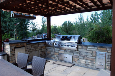Cette photo montre une très grande terrasse arrière chic avec une cuisine d'été, des pavés en pierre naturelle et une pergola.