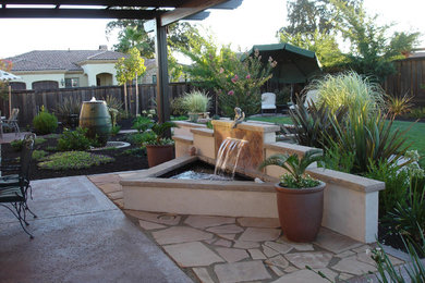 Imagen de patio clásico en patio trasero con fuente, adoquines de piedra natural y toldo