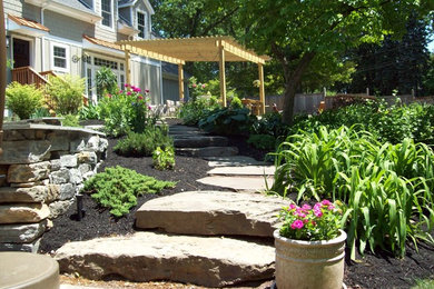 Modelo de patio campestre de tamaño medio en patio trasero con jardín de macetas, adoquines de piedra natural y pérgola