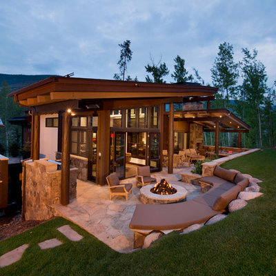Example of a large mountain style backyard stone patio design in Denver with a fire pit and a roof extension