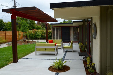 Foto de patio actual de tamaño medio en patio trasero con losas de hormigón y pérgola