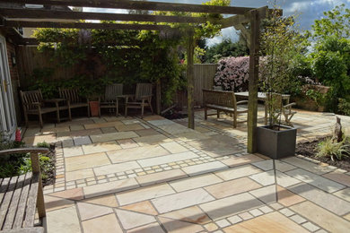 This is an example of a medium sized classic back patio in Sussex with natural stone paving and a pergola.