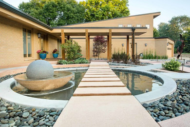 Example of a large trendy front yard patio fountain design in Other with a pergola