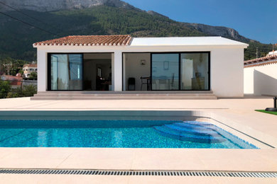 This is an example of a medium sized mediterranean front l-shaped natural swimming pool in Other with a pool house and tiled flooring.