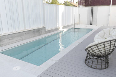 Modelo de casa de la piscina y piscina alargada actual de tamaño medio rectangular en patio delantero con suelo de baldosas