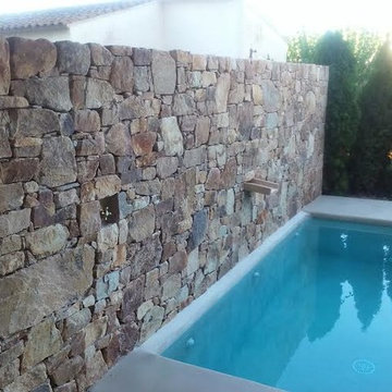 detalle de muro de piedra natural frente a piscina con cascada integrada y grifo