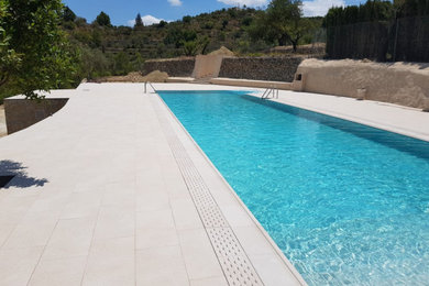 Imagen de piscina alargada mediterránea grande rectangular en patio trasero con paisajismo de piscina y suelo de baldosas
