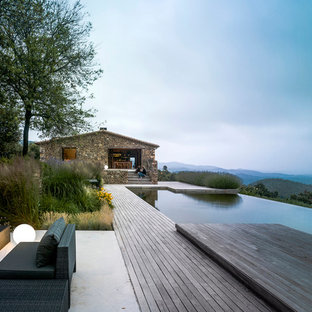 Immagine di un'ampia piscina a sfioro infinito rustica personalizzata dietro casa con fontane e pedane