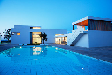 Diseño de piscina con tobogán alargada actual extra grande rectangular en patio delantero con suelo de baldosas