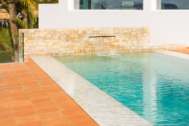 Ejemplo de casa de la piscina y piscina alargada actual grande rectangular con adoquines de piedra natural