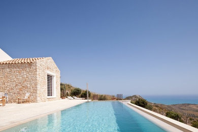 Idee per una piscina a sfioro infinito mediterranea a "L" dietro casa con pavimentazioni in pietra naturale