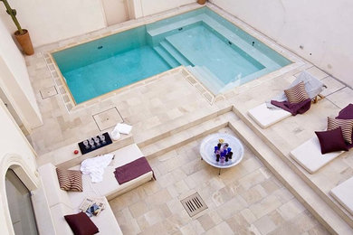 Immagine di una piscina a sfioro infinito mediterranea a "L" di medie dimensioni e nel cortile laterale con una vasca idromassaggio e pavimentazioni in pietra naturale