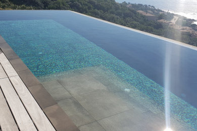 Exemple d'une grande piscine à débordement moderne rectangle avec une terrasse en bois.