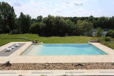 Ejemplo de piscina infinita actual grande rectangular con adoquines de piedra natural