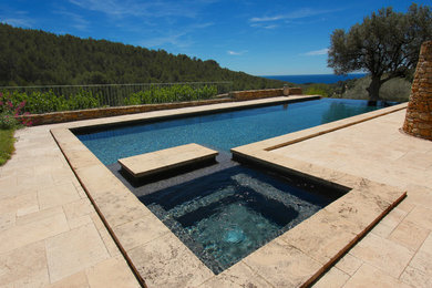 Cette photo montre une piscine à débordement tendance en L de taille moyenne avec un bain bouillonnant et des pavés en pierre naturelle.