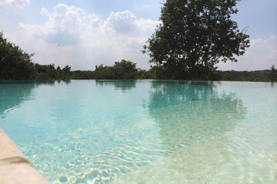 Imagen de piscina infinita contemporánea extra grande en forma de L en patio delantero con adoquines de piedra natural