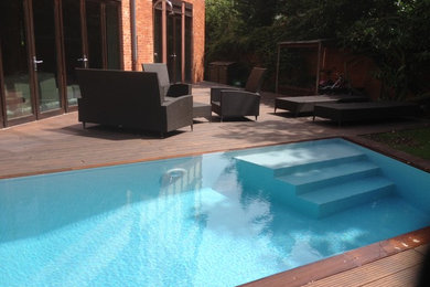 Aménagement d'une petite piscine à débordement et arrière contemporaine sur mesure avec une terrasse en bois.