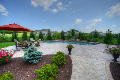 Modelo de piscina alargada clásica grande tipo riñón en patio trasero con adoquines de piedra natural