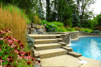 Réalisation d'une grande piscine naturelle et arrière tradition sur mesure avec un bain bouillonnant et des pavés en pierre naturelle.