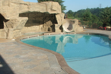 Modelo de piscina con tobogán tradicional grande a medida en patio trasero con adoquines de hormigón