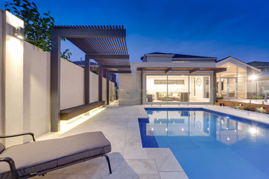 Ejemplo de casa de la piscina y piscina alargada actual de tamaño medio rectangular en patio trasero con adoquines de piedra natural