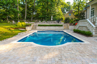Foto de piscina alargada tradicional grande rectangular en patio trasero con adoquines de piedra natural