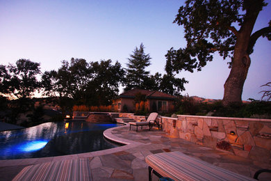 На фото: бассейн-инфинити произвольной формы на заднем дворе в средиземноморском стиле с покрытием из каменной брусчатки с