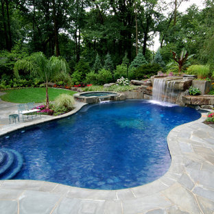 Immagine di una grande piscina tropicale personalizzata dietro casa con una vasca idromassaggio e pavimentazioni in pietra naturale