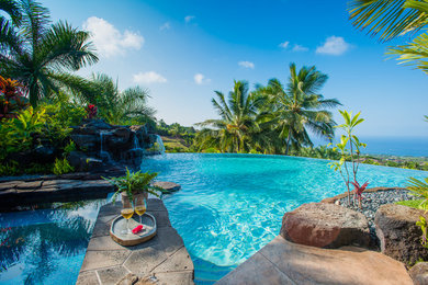 Ejemplo de piscina con fuente infinita tropical grande a medida en patio trasero con suelo de hormigón estampado