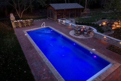 Diseño de piscina alargada clásica grande rectangular en patio trasero con adoquines de ladrillo