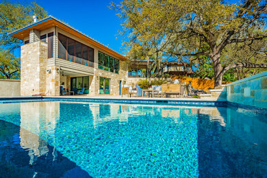 Diseño de piscina alargada actual grande rectangular en patio trasero con adoquines de piedra natural