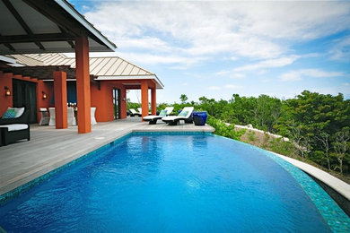 Example of a large island style backyard custom-shaped infinity pool design in Other with decking