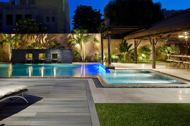 Ejemplo de piscina con fuente alargada minimalista de tamaño medio en forma de L en patio trasero con suelo de baldosas