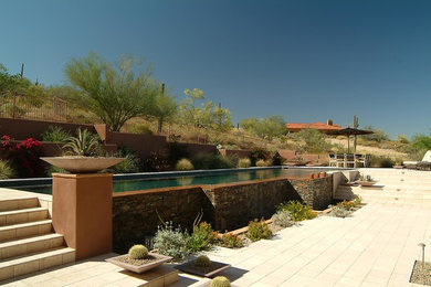 Modelo de piscina infinita mediterránea de tamaño medio rectangular en patio trasero con adoquines de piedra natural