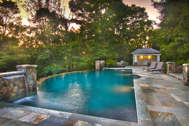 Ejemplo de piscina con fuente infinita de estilo americano grande a medida en patio trasero con adoquines de piedra natural