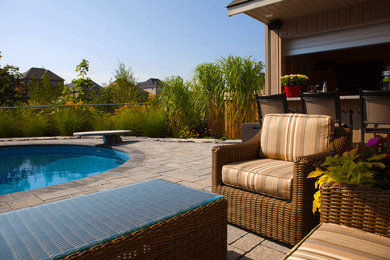 Ejemplo de casa de la piscina y piscina alargada exótica grande tipo riñón en patio trasero con adoquines de hormigón