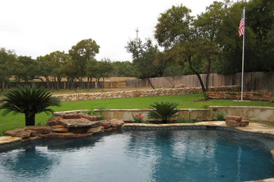 Large back custom shaped lengths swimming pool in Austin with a water feature and natural stone paving.